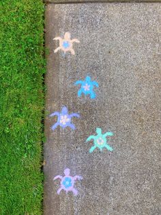 the sidewalk is painted with blue and pink turtles on it, along with green grass