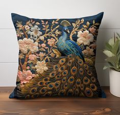 a decorative pillow with a blue peacock and flowers on it next to a potted plant