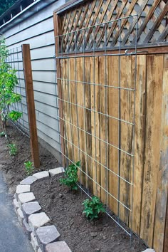 a wooden fence next to a building with plants growing out of the ground in front of it