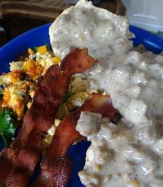 a blue plate topped with eggs, bacon and gravy next to a salad