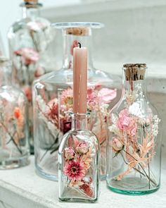 vases with flowers and candles are sitting on a ledge in front of glass bottles