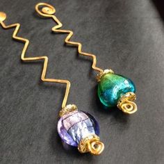 two colorful glass beads are attached to gold earwires on a black surface with the words beaded wire bookmarks written below them