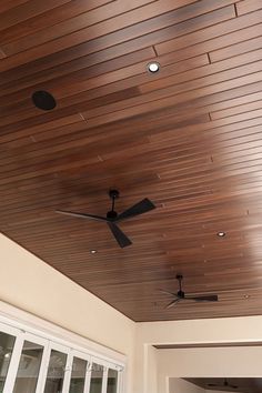 a ceiling fan mounted to the side of a wooden ceiling in a room with sliding glass doors