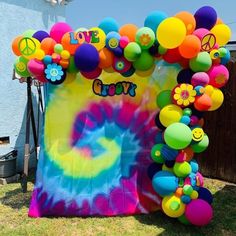 a tie - dyed backdrop with balloons and peace signs on the top, in front of a house