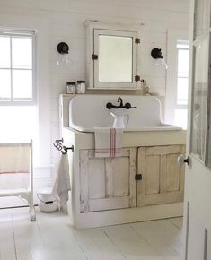 a bathroom with white walls and wooden floors has a sink, mirror, and towel rack