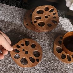 three wooden coasters with holes on them and a hand holding a cup in the middle