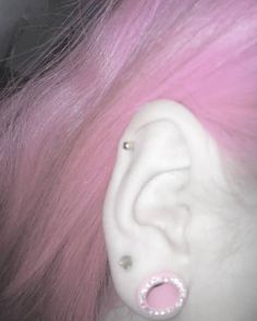 a close up of a person with pink hair and piercings on their ears,