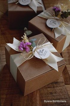 three brown boxes with white ribbons and flowers on them sitting on top of a wooden table