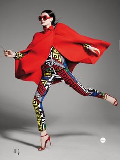 a woman in a red cape and patterned leggings is dancing with her legs spread out