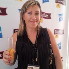 a woman holding up a glass of orange juice in front of a wall with banners on it