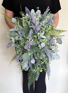 a man holding a bouquet of flowers and greenery in front of his back legs