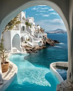 an outdoor swimming pool with blue water and white buildings on the cliff side, overlooking the ocean