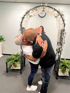 a man and woman hug each other in front of an arch decorated with greenery