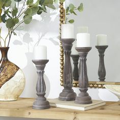 some candles are sitting on a table next to a mirror and vase with greenery in it