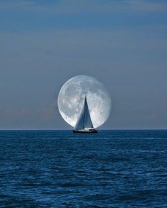 a sailboat floating in the ocean under a full moon