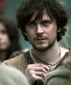 a man with long hair and blue eyes is standing in front of other people wearing necklaces