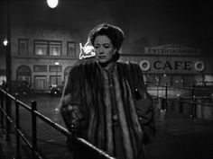 a woman in a fur coat is walking down the street with her hand on her hip