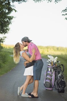 a man and woman kissing on the side of a road with golf bags behind them