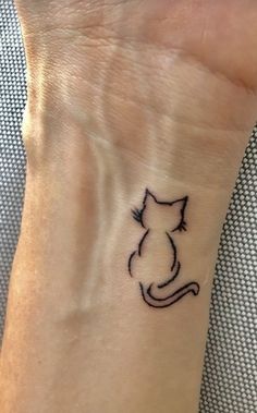 a cat tattoo on the wrist of a woman's hand, with black ink