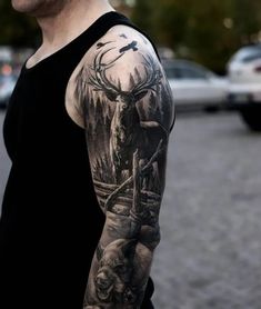 a man with a deer tattoo on his arm is standing in front of some cars