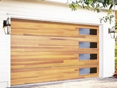 a large wooden garage door in front of a white house with plants on the side