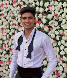 a man wearing a white shirt and black bow tie standing in front of a flower wall