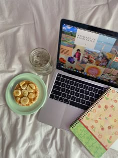 an open laptop computer sitting on top of a bed next to a plate of food