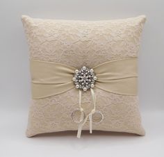 the ring pillow is adorned with a ribbon and jeweled brooch on it's side