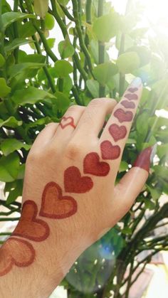 a person's hand with hearts painted on it holding up a potted plant