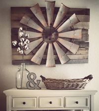 a white dresser topped with a basket filled with flowers next to a wall mounted windmill