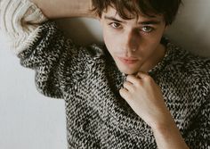 a young man is posing for the camera with his hand on his head and wearing a sweater