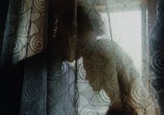 the silhouette of a person standing in front of a window covered with sheer curtaines