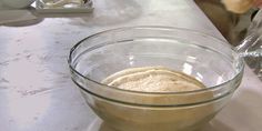 a person mixing something in a glass bowl on top of a white tablecloth covered counter