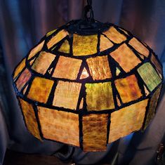 a stained glass lamp hanging from a metal rod on a curtained window sill