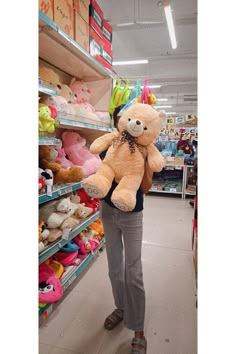 a woman is holding a large teddy bear in a store with other stuffed animals on the shelves