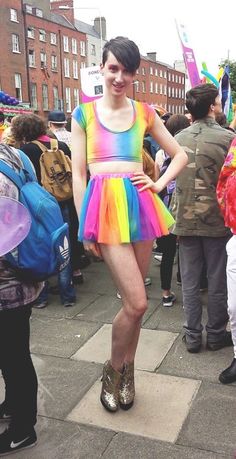 a woman in a rainbow dress standing on the sidewalk