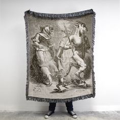 a person holding up a tapestry with two men on it