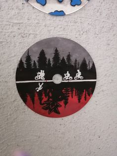 there is a cd disc on the wall next to a clock that has trees and bicycles on it