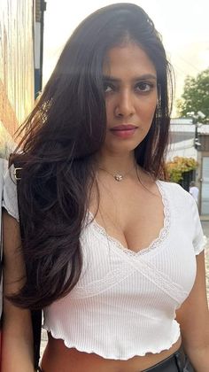 a woman with long dark hair wearing a white top and black leather skirt posing for the camera