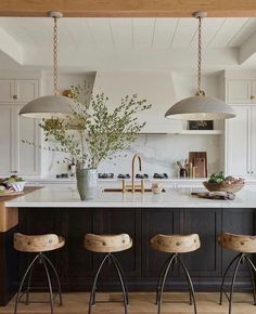 three stools sit in front of a kitchen island with marble counter tops and pendant lights