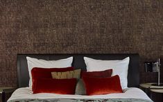 a bed with two red pillows on top of it next to a night stand and lamp