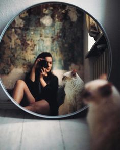 a woman sitting on the floor in front of a mirror with a cat looking at her