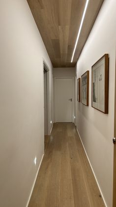 an empty hallway with white walls and wood floors is seen in this image, there are two framed pictures on the wall