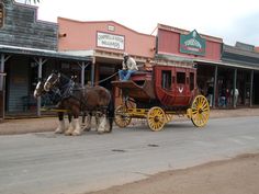 two horses are pulling a carriage down the street in front of shops and businesses on a cloudy day