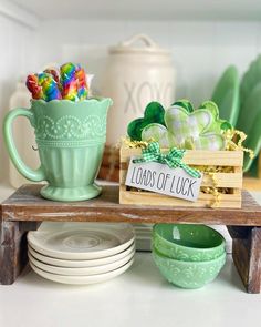 a table topped with lots of green dishes and cups filled with candies next to a sign that reads loads of luck