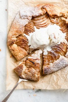 an apple pie with whipped cream on top is cut into slices and sits on a piece of parchment paper