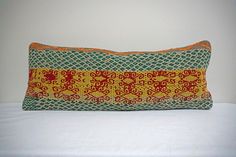 an orange and green pillow sitting on top of a white bed next to a wall