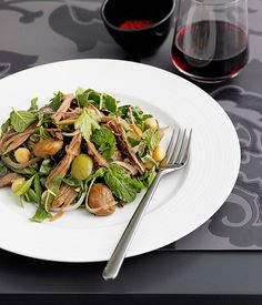 a white plate topped with salad next to a glass of wine