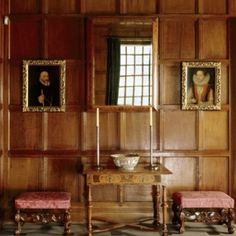 a room with wooden paneling and paintings on the wall, two chairs in front of a table