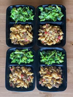 four black plastic trays filled with food on top of a wooden table next to each other